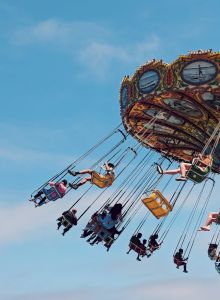 The image shows people enjoying a swing ride (chair-o-planes) at an amusement park set against a clear blue sky, conveying a sense of fun and motion.