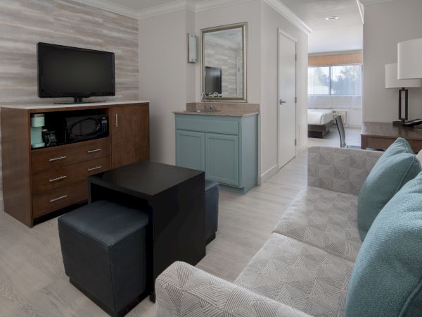 A modern living space with a sofa, TV, microwave, coffee table, and a view into an adjoining bedroom area.