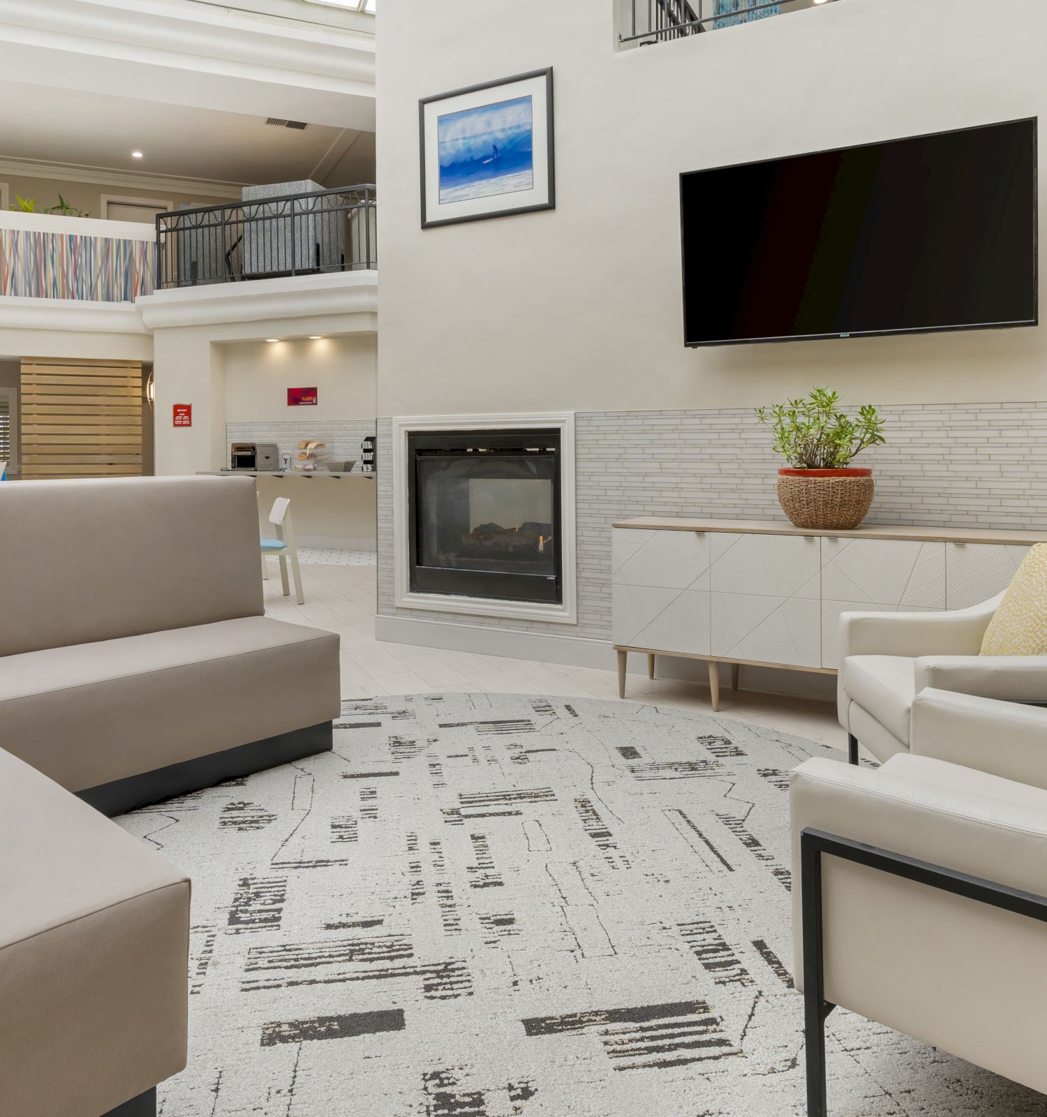 A modern living room with a sectional sofa, armchairs, a TV, and a fireplace. Decor includes a potted plant and framed artwork on the walls.