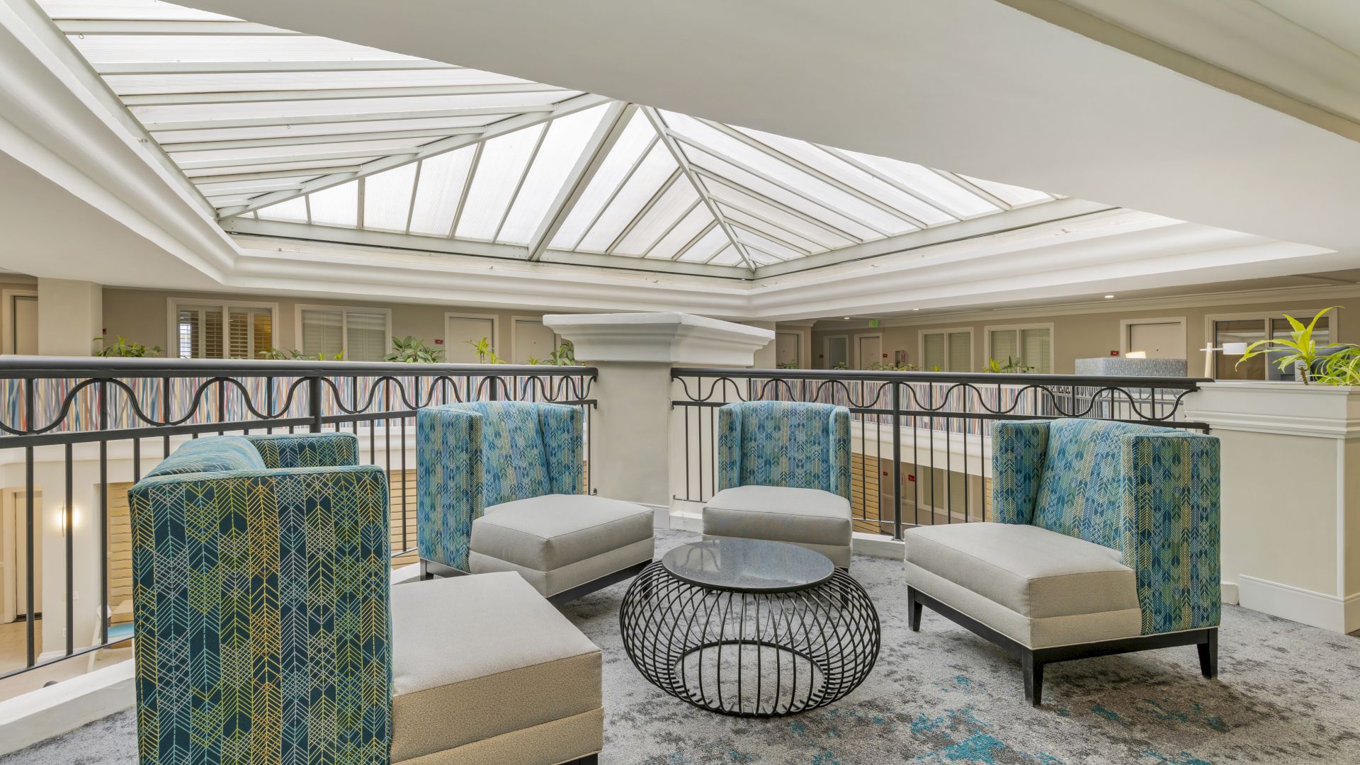A sitting area with four cushioned chairs, a round glass-top table, and a skylight overhead in a bright, modern space.