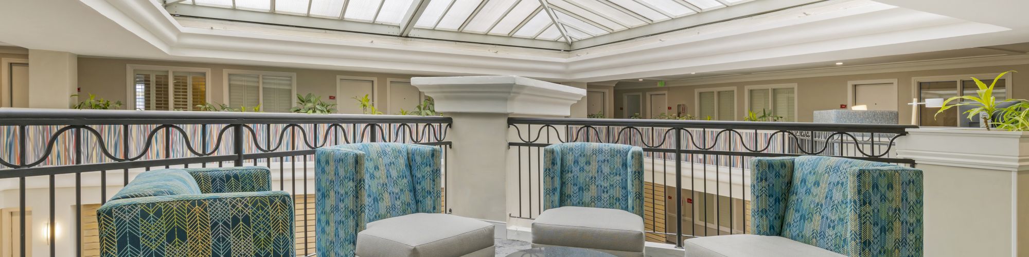 A sitting area with four cushioned chairs, a round glass-top table, and a skylight overhead in a bright, modern space.