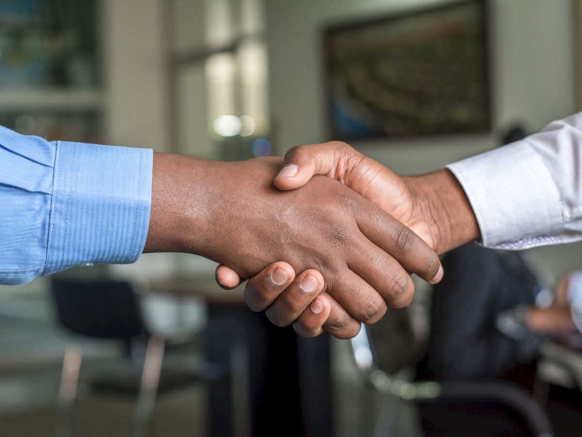 Two people are shaking hands in an office setting, symbolizing a business agreement or partnership.