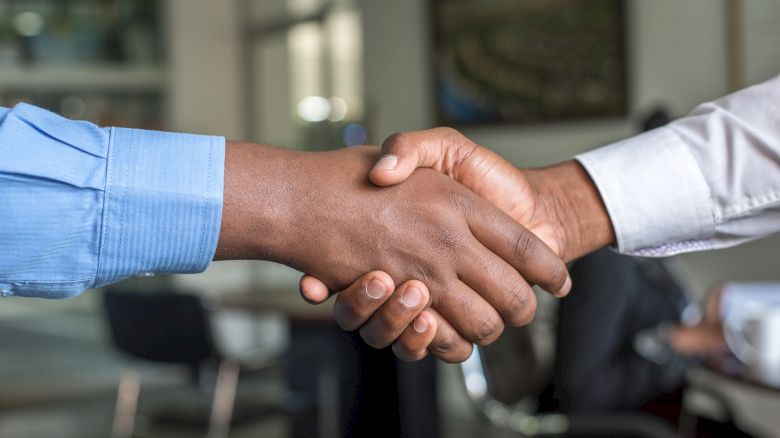 Two people are shaking hands in an office setting, symbolizing a business agreement or partnership.