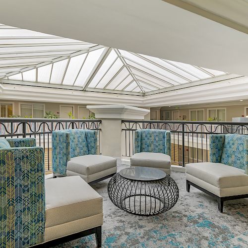 This image shows a sitting area with patterned chairs and a round table under a skylight in a spacious, well-lit indoor setting, probably an atrium.