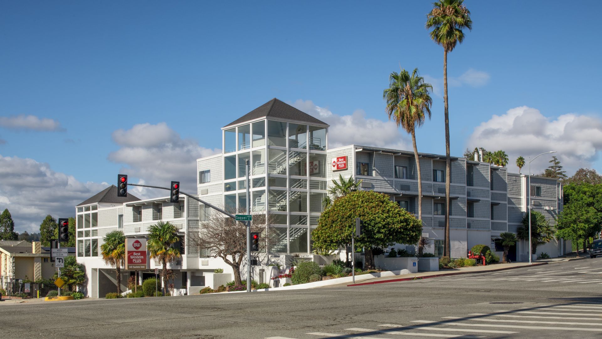 The image shows a modern multi-story building with large windows, palm trees, and a street intersection with traffic lights and crosswalks ending the sentence.