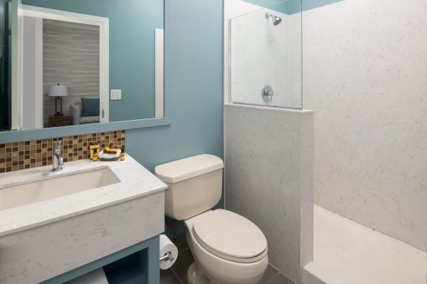 A modern bathroom with a shower, toilet, and sink, featuring a rectangular mirror, light blue walls, and a tiled backsplash.