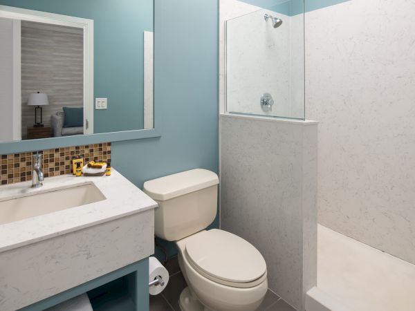A modern bathroom with a shower, toilet, and sink, featuring a rectangular mirror, light blue walls, and a tiled backsplash.