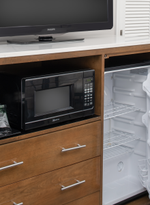 A mini fridge, microwave, and coffee maker are in a cabinet with a TV on top. The fridge door is open, and there's a shelf with drawers.