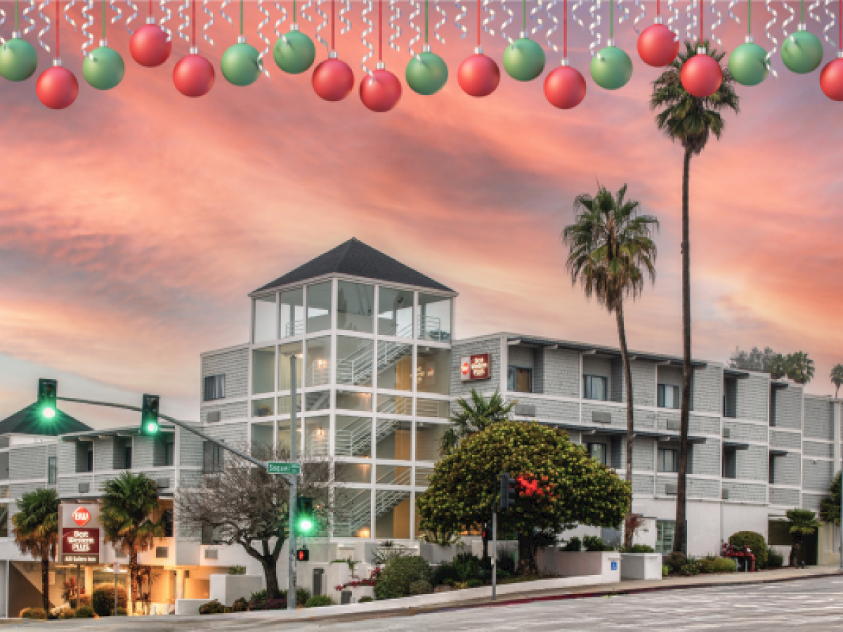 A coastal-style hotel or building at sunset with palm trees, streetlights, and a festive or holiday topper across the top of the image.